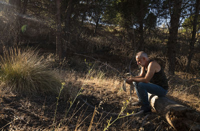 Side view of adult man sitting on tree trunk on land