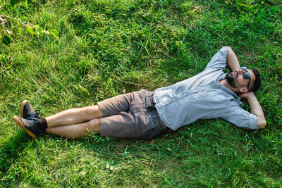 Young handsome sports european man in sunglasses is resting on a grass in summer park, top view.