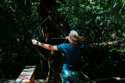 Full length of man holding bow in forest