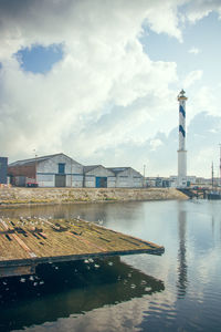 View of lighthouse by buildings against cloudy sky 