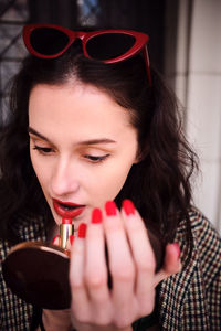 Woman applying lipstick while looking in hand mirror