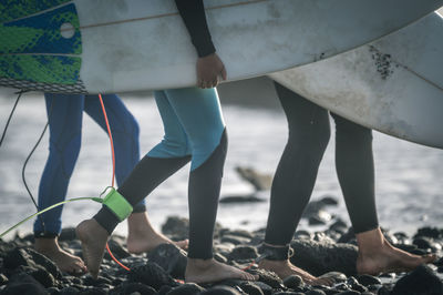 Low section of people holding surfboards at beach