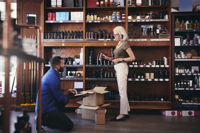 Saleswoman showing beauty product to male colleague while standing by rack in deli