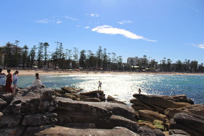 People on rocks by sea against sky