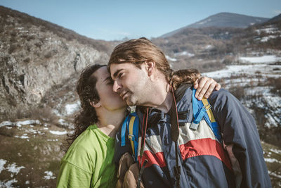 Woman kissing man while standing on mountains against sky