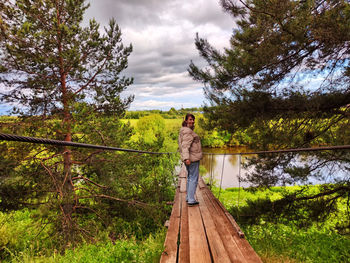 Rear view of woman standing on footbridge against trees