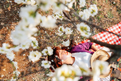 High angle view of woman napping while lying on land seen through blossoms