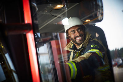 Smiling firefighter sitting in fire engine seen through glass window