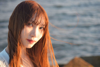 Close-up portrait of young woman with sea in background