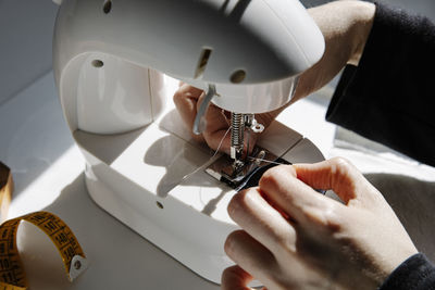 Crop seamstress threading a sewing machine needle at home workshop