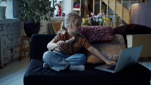 Full length of girl using laptop while sitting on sofa