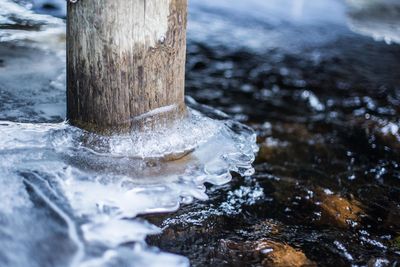 Close-up of wooden post amidst frozen ice during winter