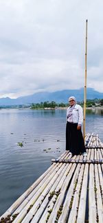 Full length of woman standing on wooden raft in lake against sky