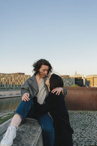 Lesbian couple embracing on rooftop against clear sky