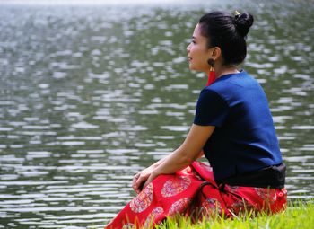 Side view of young woman sitting by lake