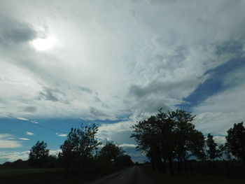 Empty road amidst trees against cloudy sky