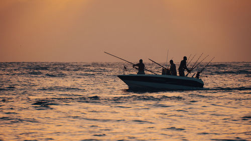 Silhouette people in boat on sea against sky during sunset