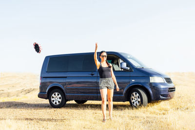 A happy young woman in a caravan in a rural landscape throwing her hat