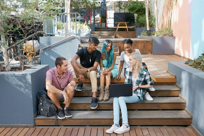 Full length of friends sitting on steps in campus