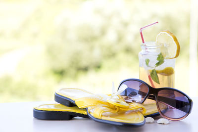 Close-up of sunglasses slippers and drink on table