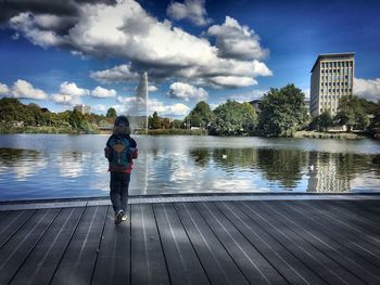 Boy standing by lake against sky