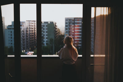 Rear view of woman standing by window in city