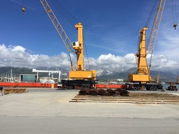 Cranes at harbor against cloudy sky