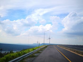 Windmills by road against cloudy sky