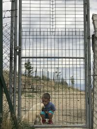 Boy sitting on metal fence