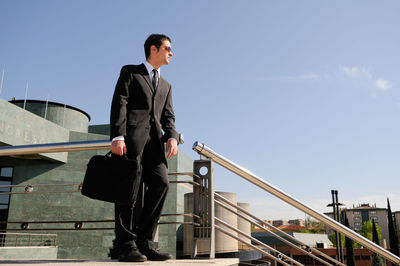 Low angle view of businessman standing against blue sky