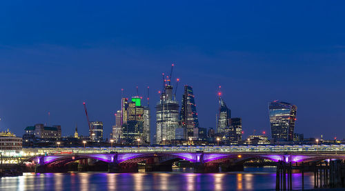 Illuminated buildings by river against sky at night