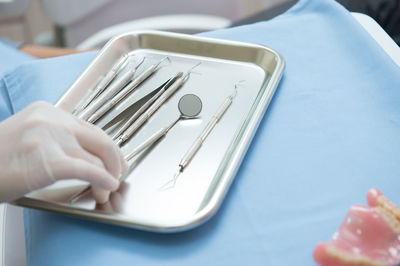 Cropped hand of dentist holding dental equipment in tray on table