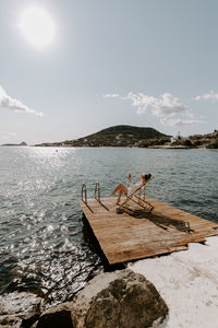 Rear view of woman sitting on pier by sea