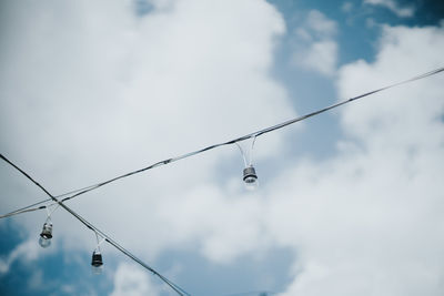 Low angle view of light bulbs against cloudy sky