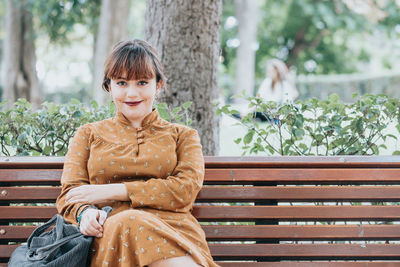 Portrait of young woman sitting on bench at park