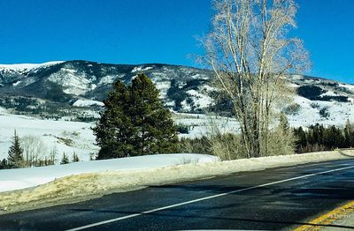 Snow covered road by trees against clear blue sky