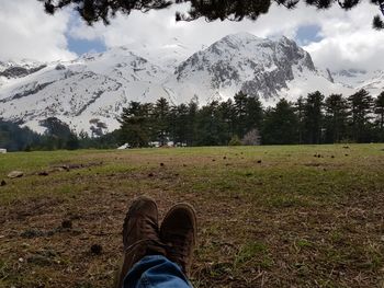 Low section of man resting on grass against snowcapped mountain and sky