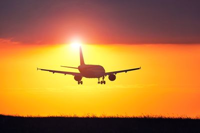 Silhouette airplane flying against sky during sunset