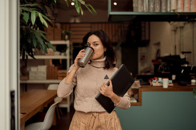 Portrait of businesswoman drinking coffee while holding laptop at cafe