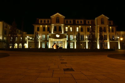 Illuminated street by buildings against sky at night