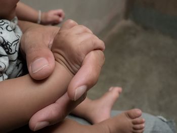 Midsection of parent holding baby hand at home