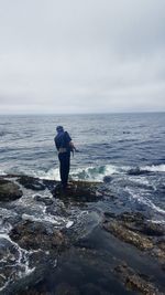 Rear view of man standing in sea against sky