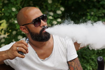 Man smoking electronic cigarette against plants