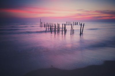 Wooden posts in sea against sky at sunset