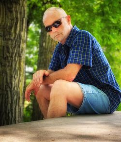 Man wearing sunglasses sitting on a park bench enjoying a beautiful day in the park. 