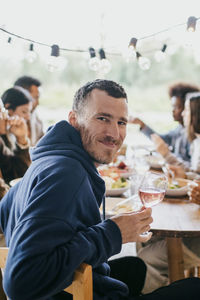 Portrait of smiling mature man sitting with wineglass at dinner party in patio