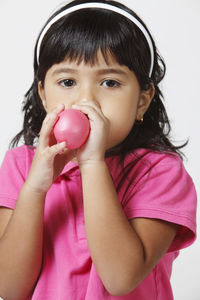 Portrait of cute girl blowing balloon over white background