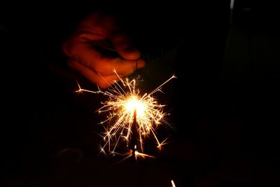 Cropped hand holding lit sparkler at night