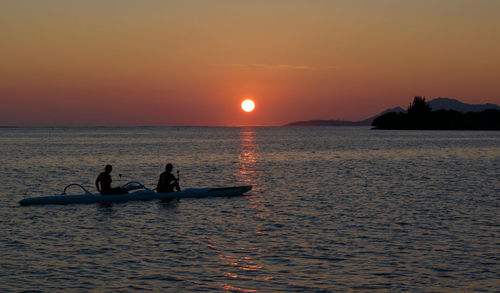 Silhouette people on sea against sky during sunset