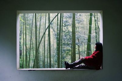 Side view of woman sitting on window